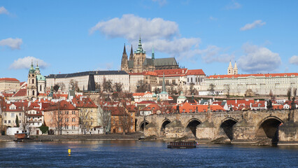 Obraz premium Prague Castle and Charles Bridge along Vltava River with red rooftops and blue sky