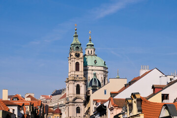 Obraz premium St Nicholas Church Prague with copper dome rising above red rooftops and blue sky
