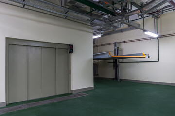 Obraz premium An elevator is present in a building with a parking system nearby. The area has a clean floor and is well-lit. The elevator doors are closed, and a green light is on