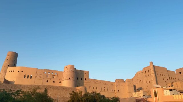 Historic Bahla Fort built with traditional mud architecture standing on rocky ground under clear blue sky showing ancient Omani heritage. Bahla, Oman - February 17 2026