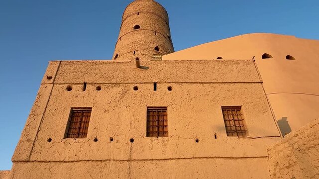 Historic Bahla Fort built with traditional mud architecture standing on rocky ground under clear blue sky showing ancient Omani heritage. Bahla, Oman - February 17 2026