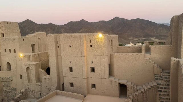 Historic Bahla Fort built with traditional mud architecture standing on rocky ground under clear blue sky showing ancient Omani heritage. Bahla, Oman - February 17 2026
