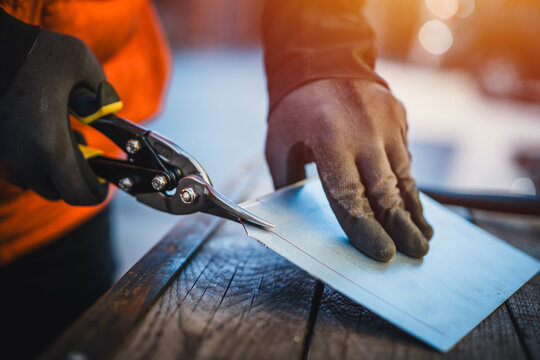 A man cuts a metal sheet with metal shears, construction work. Sheet metal shears snips cut edge of galvanized steel from roofing iron, outdoor work.