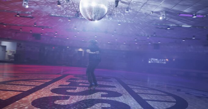 Cinematic wide, steady cam shot of professional skater doing impressive spin move under disco ball with fog