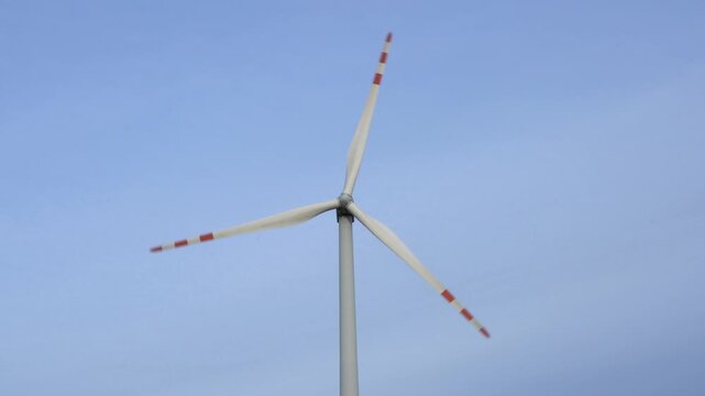 A majestic wind turbine with its blades in motion, set against a vast expanse of clear blue sky, symbolizing renewable power generation