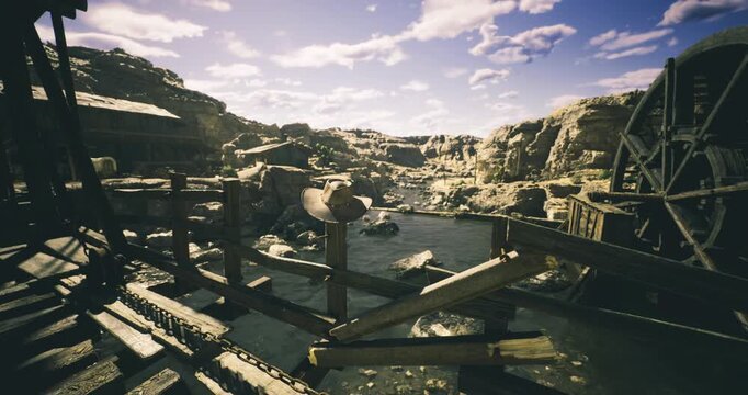 An old mining area features rustic wooden structures alongside a serene river. Rocky terrain and overcast sky create a hauntingly beautiful atmosphere in the landscape.