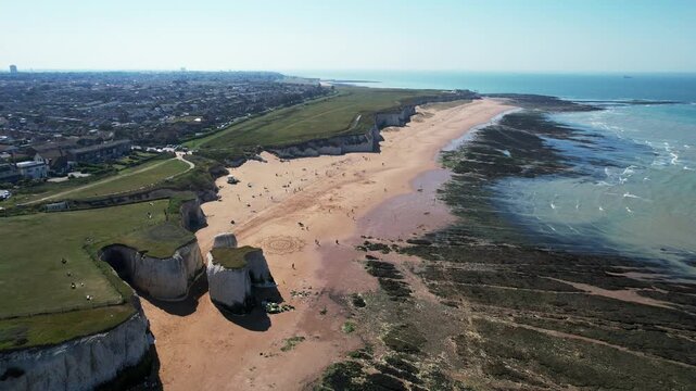 Drone Aerial view of coastline with sandy beach meeting the atlantic ocean. Waves create patterns over dark rocks and green algae. Margate botany beach Kent United Kingdom
