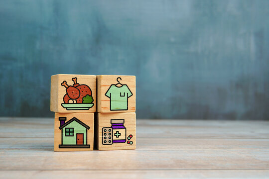 Basic human needs concept with wooden blocks showing icons of food, clothing, housing and medicine on wooden table.