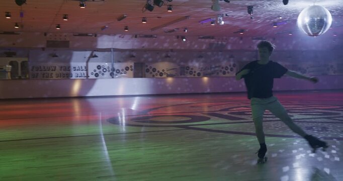 Young man doing awesome leg up spin trick across empty disco floor - steady cam tracking shot