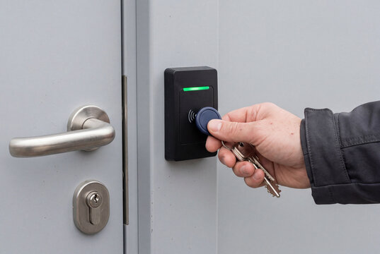 Person using a blue key fob on an electronic door lock. The reader displays a green light. Close up.