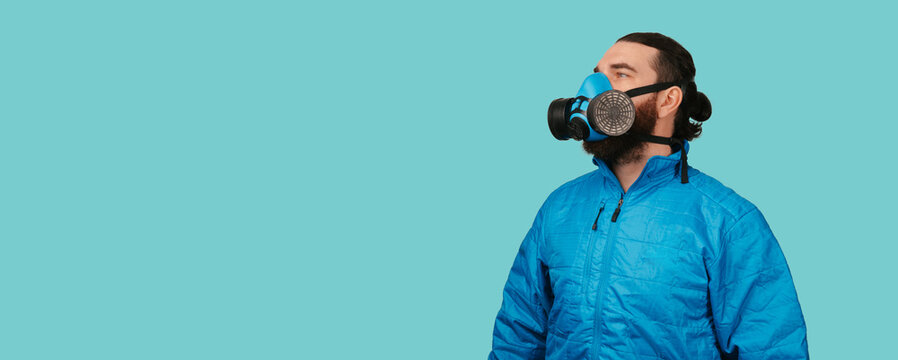 Man Wearing Respirator And Blue Jacket Gazes Upward Against Teal Background, Studio Portrait Conveying