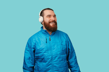 Obraz premium Caucasian Man Wearing Headphones, Relaxed And Smiling While Dressed In Blue Jacket On Turquoise Background