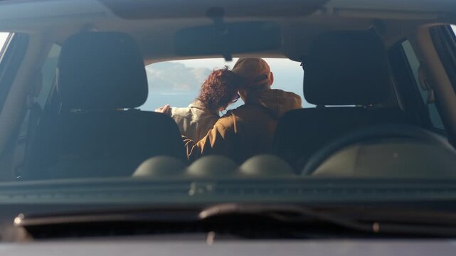 Senior couple hugging enjoying the view. Rear view of an affectionate senior couple embracing and looking at the sea from the back of their car during a road trip, enjoying a romantic moment