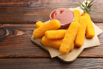 Fototapeta premium Tasty fried cheese sticks, ketchup and rosemary on wooden table, closeup. Space for text