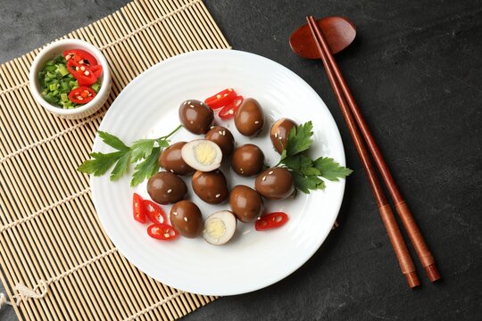 Pickled quail eggs, chopsticks and ingredients on black table, flat lay
