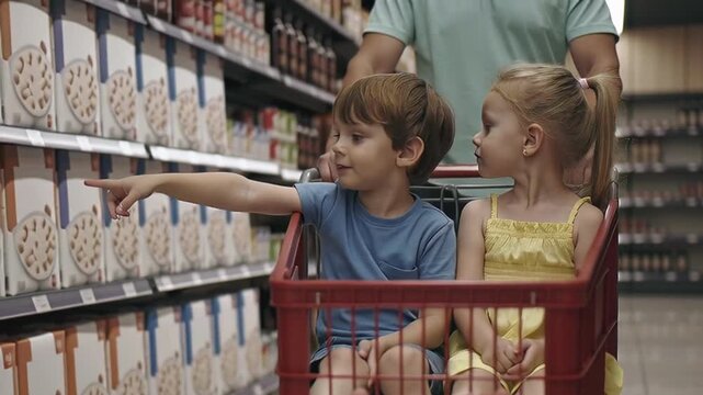 Young boy pointing at cereal boxes in a supermarket shopping cart while a girl observes, with a parent pushing them through an aisle, family shopping concept