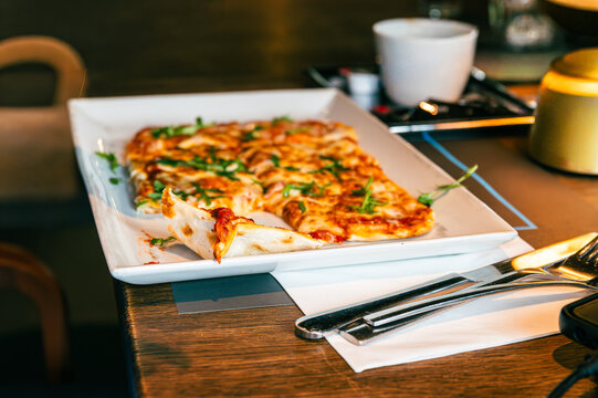 Freshly baked German Flammkuchen served on a white rectangular plate in a restaurant. Traditional Tarte Flambee with melted cheese and green herbs, close,Homemade Flammkuchen pizza on a restaurant tab