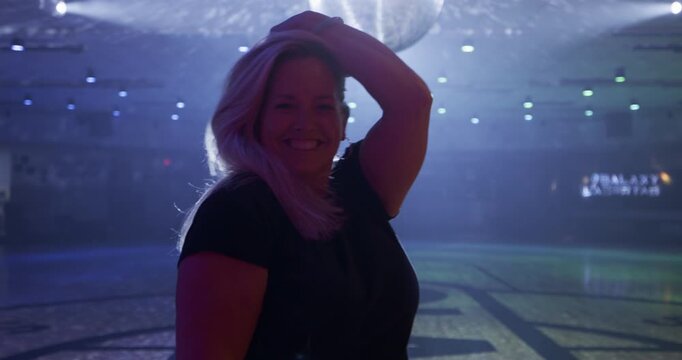 Blonde woman on disco floor attempting hair flip for camera - medium shot