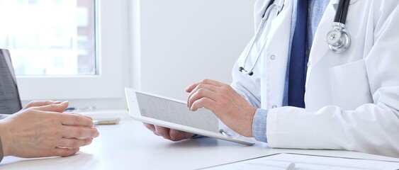 Close-up of doctor man showing information on tablet to patient woman during medical visit,...