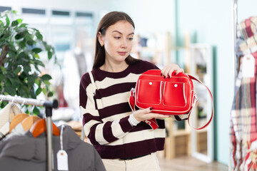 Fashionable young female client standing against background of shelves with clothes in modern store...