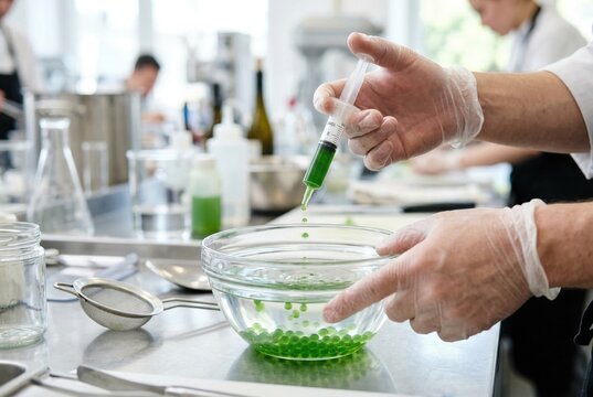 Chef using syringe to drop green liquid into bath for molecular gastronomy spherification