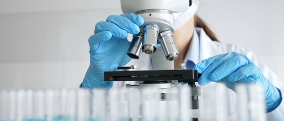 Laboratory scientist wearing blue protective gloves carefully positioning microscope slide,...