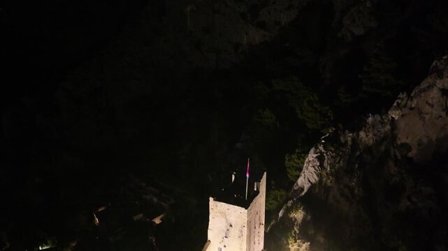 Historic Mirabela fortress tower rising above Omis old town during night.