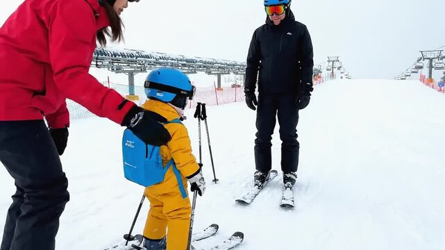 Family enjoys skiing together as mother assists child in learning to ski on snowy slope with ski lift in the background