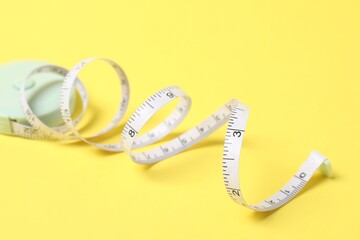 One measuring tape on yellow background, closeup