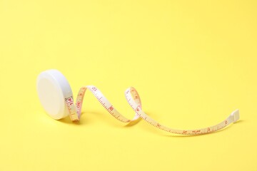 One measuring tape on yellow background, closeup