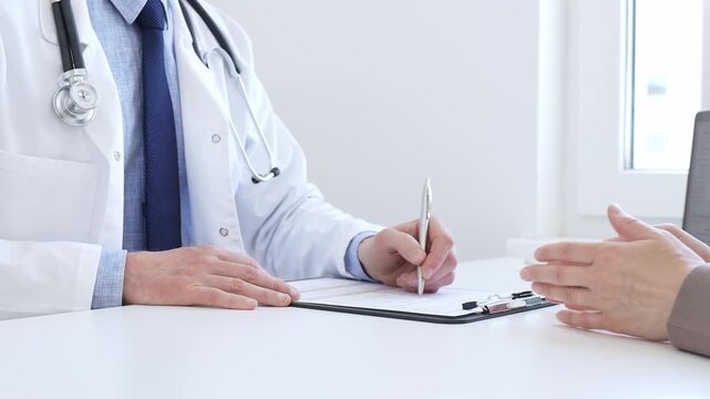 Doctor man taking notes while listening to a female patient explaining her symptoms during a medical consultation in the clinic office. Medicine and health care concept