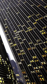Tall buildings stand side by side at night with many windows lit up. The city skyline shows a blend of structures. A view upwards highlights the patterns of lights in the windows.