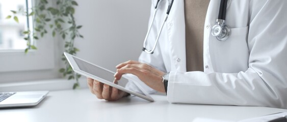 Doctor man wearing lab coat and stethoscope using digital tablet in modern medical office, browsing...