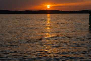 Intense fiery sunset with golden sun path reflecting on dark rippling sea surface and hill silhouette in deep orange sky. Concept of romantic evening mood, mystery and raw natural power.