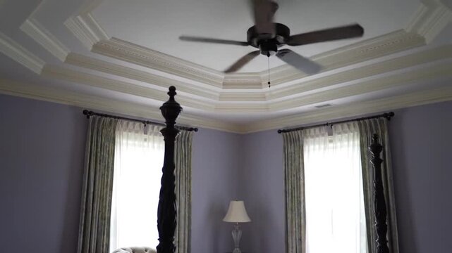 A serene bedroom with a four-poster bed and ceiling fan in a cozy video setting