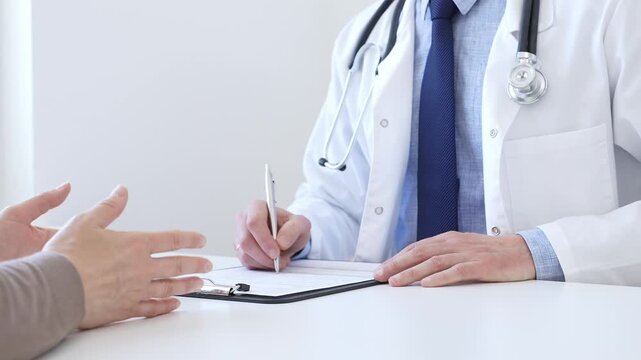 Doctor man taking notes while listening to a female patient explaining her symptoms during a medical consultation in the clinic office. Medicine and health care concept