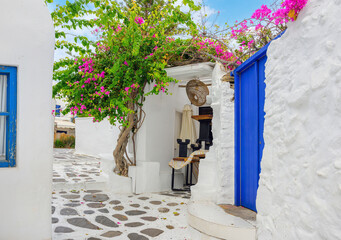 A picturesque whitewashed alley with blue door and window accents and pink bougainvillea flowers in...