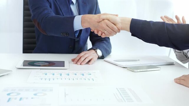 Business partners shaking hands at a meeting, celebrating successful negotiations and signing a contract, with documents, digital tablet, and smartphone on the table. Handshake close up