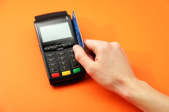 Woman with credit card using payment terminal on orange background, above view