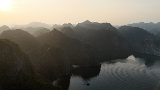 Beautiful sunrise over Ha Long Bay with limestone karst islands rising from the emerald water, traditional boats sailing between the cliffs in northern Vietnam.