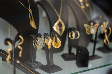 elegant display of contemporary gold jewelry on black stands featuring geometric necklaces, textured hoop earrings, and a delicate butterfly pendant in a shop window © Laurentiu Bratu