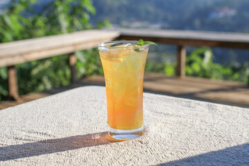 Orange juice with ice on top with mint leaf. Refreshing summer drink on linen fabric tablecloth with mountain background. © Warunporn