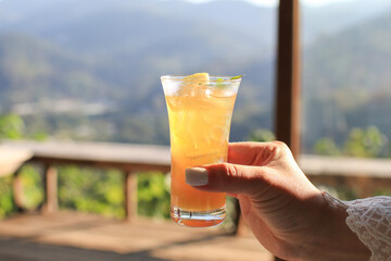 Orange juice with ice on top with mint leaf. Refreshing summer drink on linen fabric tablecloth with mountain background. © Warunporn