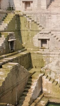 Toorji Ka Jhalra Baoli stepwell and water storage inside it - one of water sources in Jodhpur, Rajasthan, India. Sunny day, water ripples reflect walls of the pool. Camera vertical pan