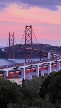 View of Lisbon view from Miradouro do Bairro do Alvito tourist viewpoint of Tagus river, traffic on 25th of April Bridge, and Christ the King statue in the evening twilight. Lisbon, Portugal