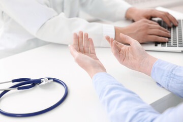 National health service (NHS). Woman having appointment with doctor at white desk indoors, selective focus
