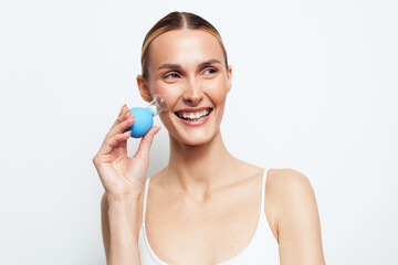 Naklejka premium Smiling woman with clear skin using a facial cleansing brush on white background. Concept of skincare, beauty, personal care, and healthy lifestyle. Bright studio lighting highlights natural look.