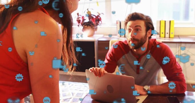 Diverse coworkers leaning at desk in office woman in red dress sharing laptop prints with icons