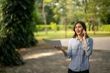 Businesswoman talking on phone and holding documents outdoors © Apichat