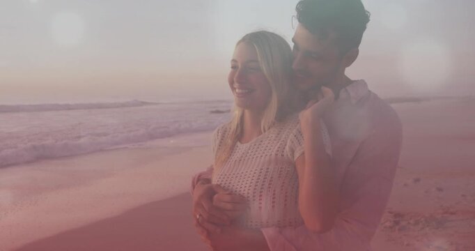 Man approaching wrapping woman behind, leaning smiling toward horizon, waves and lens flare romance